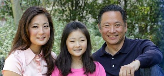 Mutsuko Adachi in a light pink shirt with her daughter in a dark pink t-shirt and her husband in a dark blue shirt.